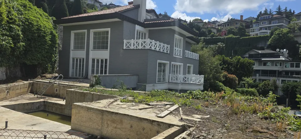 Gri ahşap kaplama cepheli villa, beyaz çapraz korkuluklu balkonlar ve boş havuz