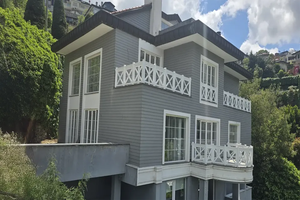 Villa cephesinde gri yatay ahşap kaplama ve beyaz çapraz desenli korkuluklar