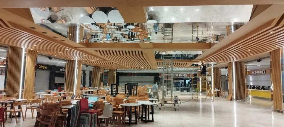 Yemek alanında yığılı sandalyeler arasında seyyar iskeleyle süren tavan montajı