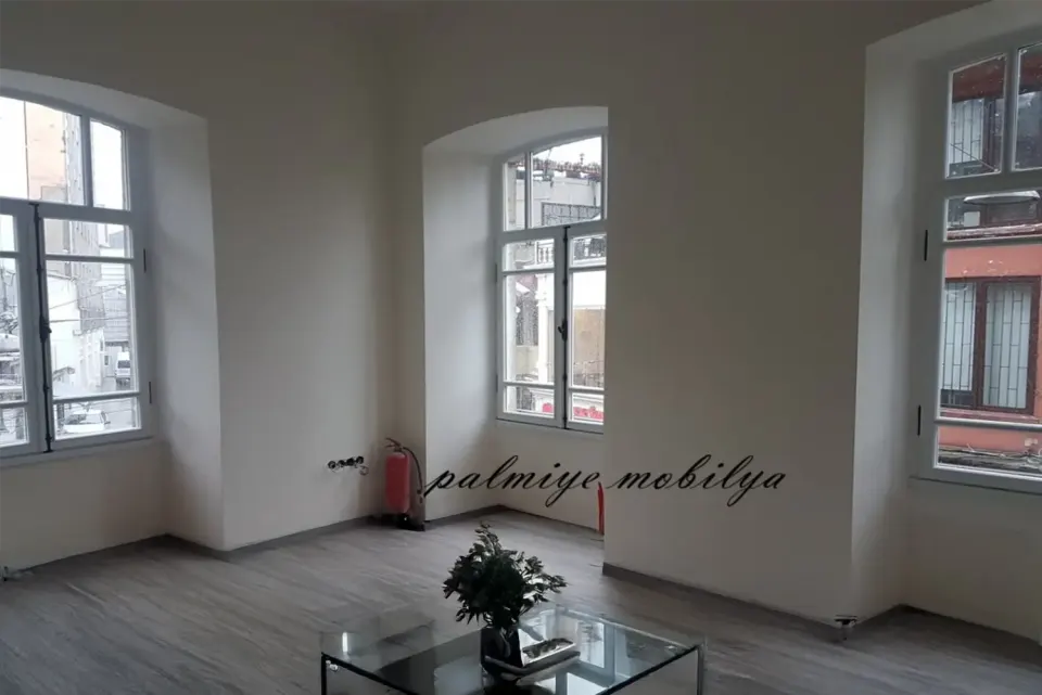 Tarihi binadaki yüksek tavanlı salonda kemerli pencereler ve cam sehpa