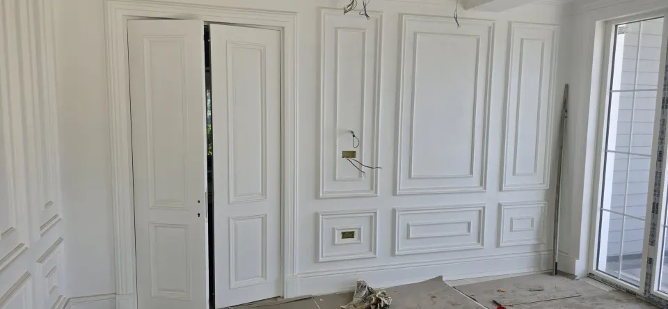 Çift kanatlı beyaz panel kapı ve yanında çerçeveli duvar panelleriyle villa odası