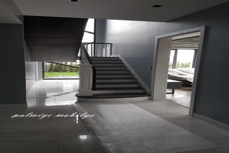 Konut dekorasyonunda koyu basamaklı beyaz merdiven ve geniş beyaz kapı kasasıyla villa holü